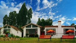 A two-story house with a stone wall, a red bench, and an orange umbrella. - Hotel Cabañas San Cayetano (Paipa)