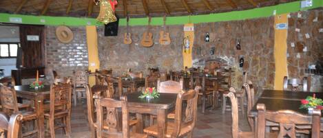 Un restaurante con mesas y sillas de madera, una pared de piedra y un techo de paja.