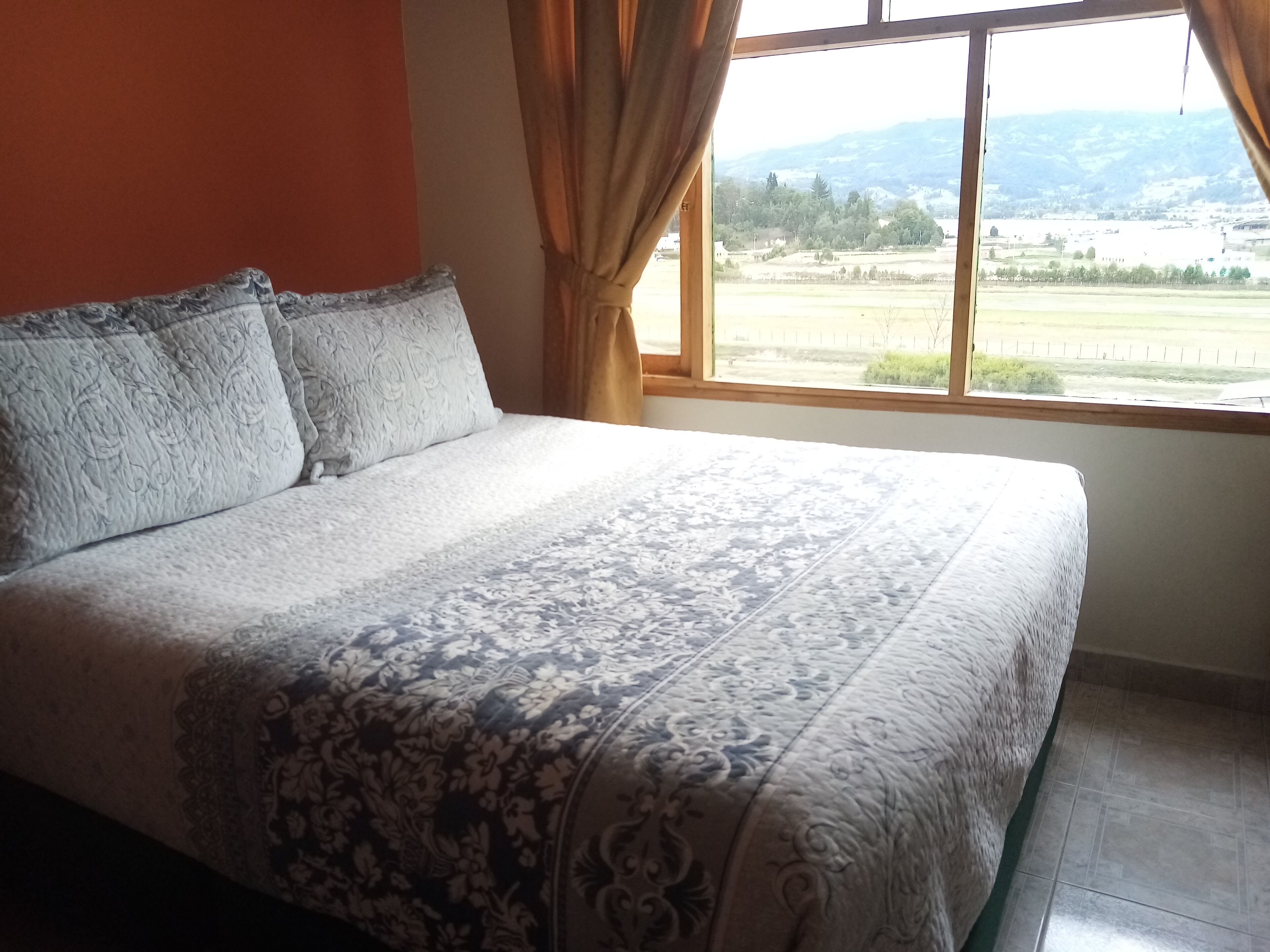 Un dormitorio con una cama grande, una ventana con cortinas y vistas a un paisaje.