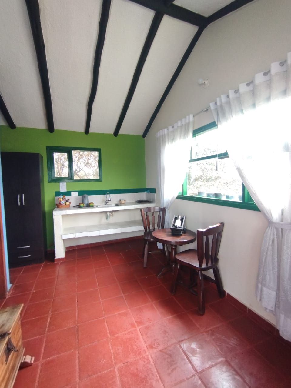 Cozinha compacta com área de refeições, janela com cortinas e chão de azulejos vermelhos.