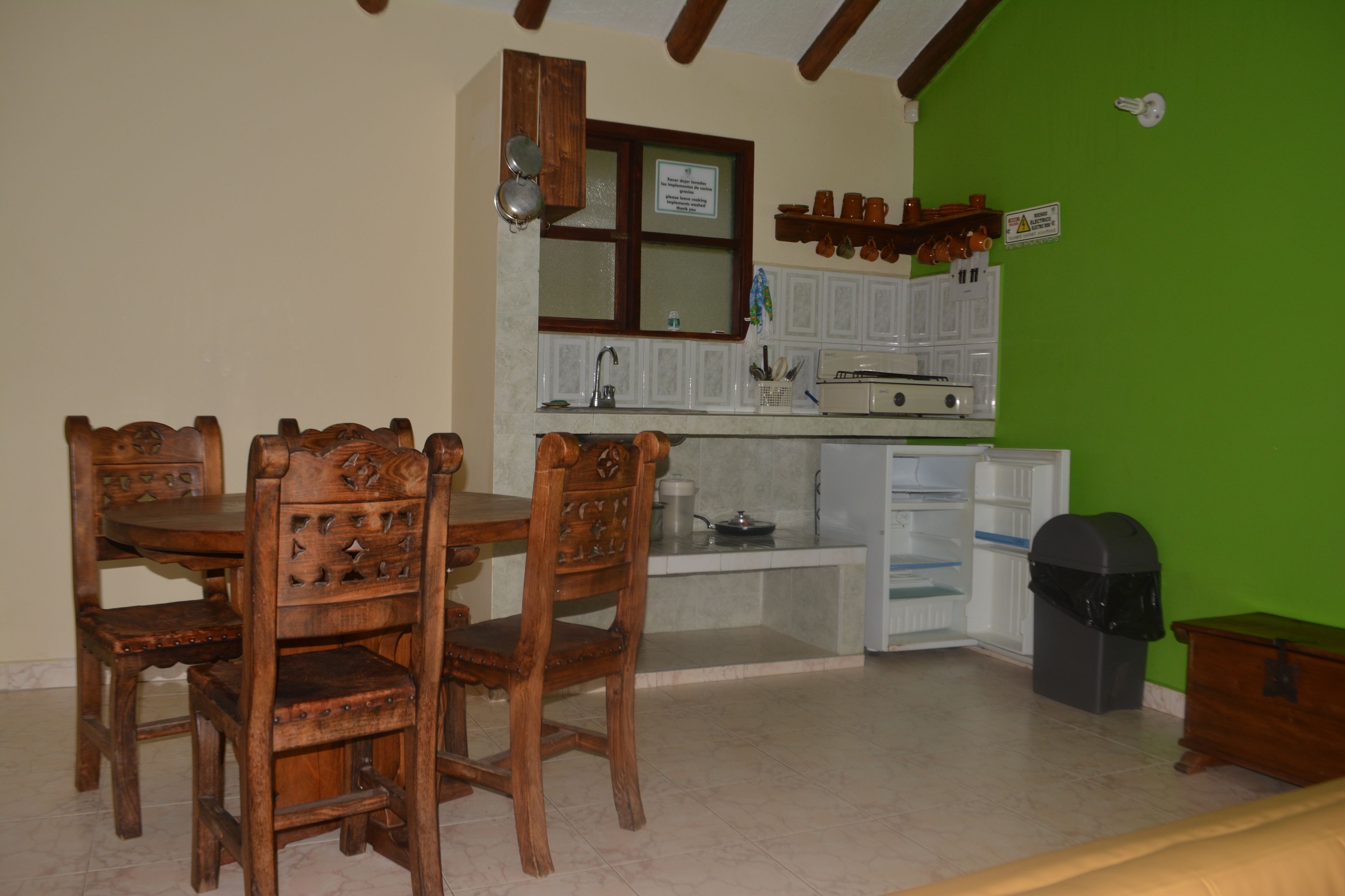 Un coin repas avec une table et des chaises en bois, une cuisine avec des meubles blancs, une fenêtre et un mur vert.
