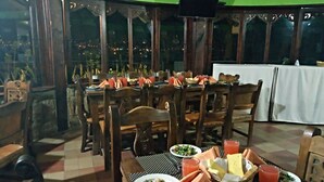 A restaurant with wooden tables and chairs, a green ceiling, and a view of the city at night. - Hotel Cabañas San Cayetano (Paipa)