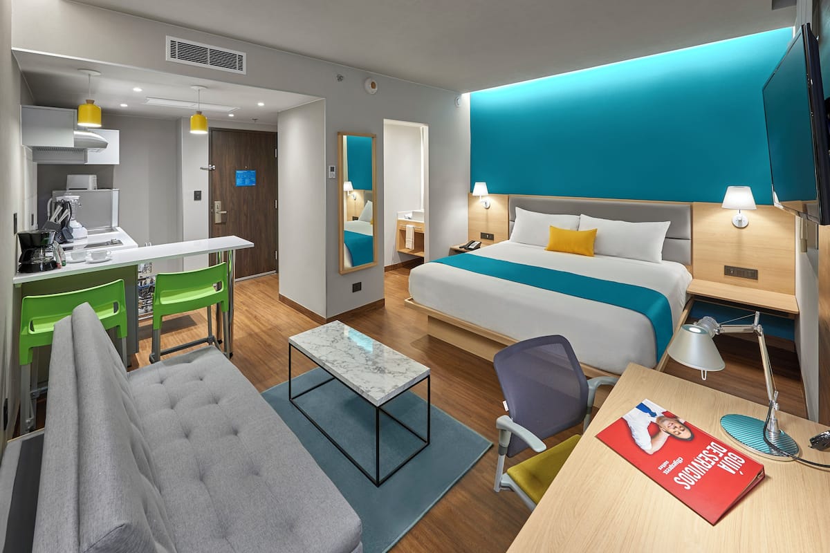 Ein Hotelzimmer mit Bett, Schreibtisch, Stuhl, Sofa, einem kleinen Tisch und einem Fernseher.