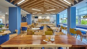A modern dining area with wooden tables and chairs, a central seating area, and large windows allowing natural light. - City Express Plus by Marriott Cancún Aeropuerto Riviera (Cancun)