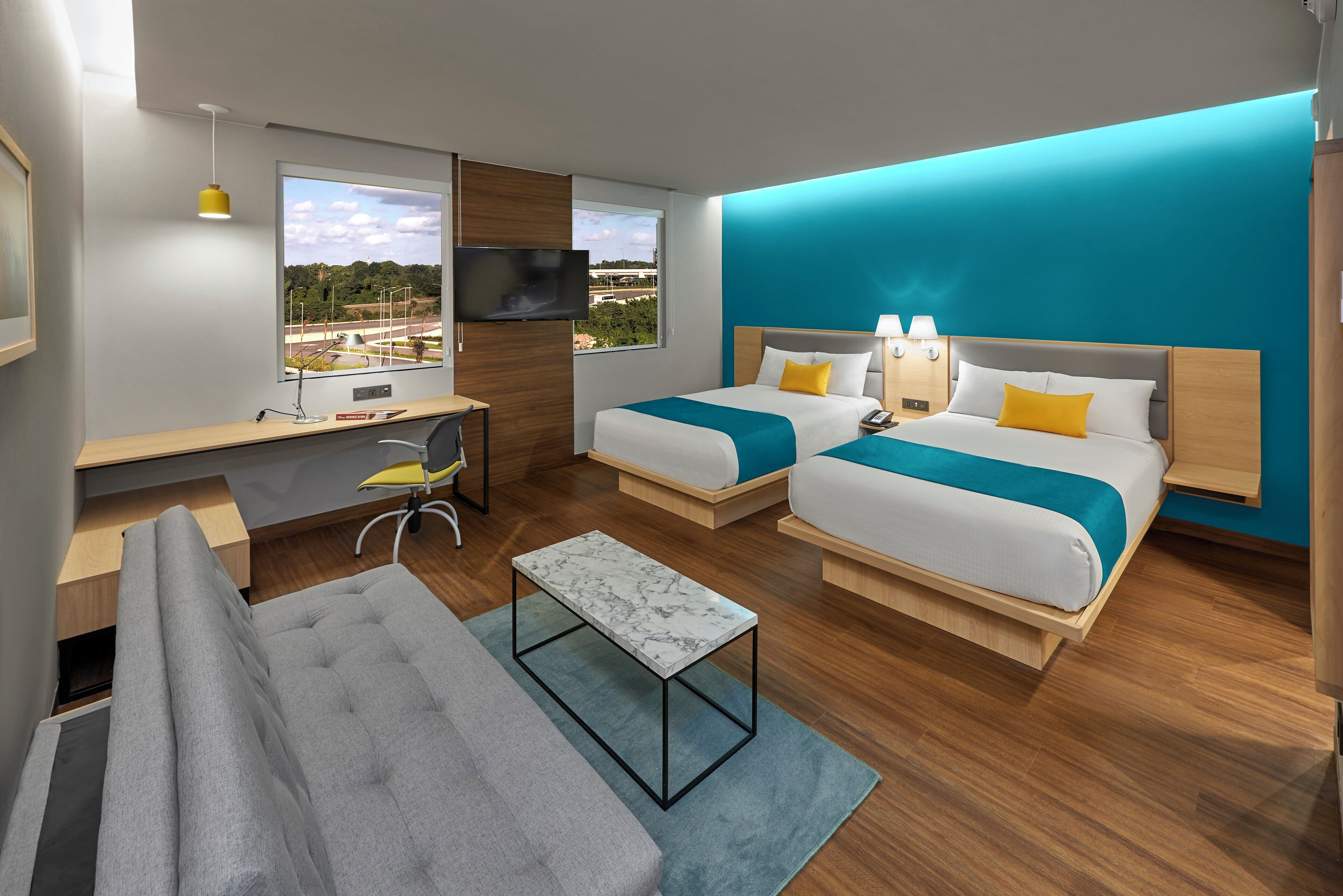 A modern hotel room with two beds, a desk, a sofa, and a TV.