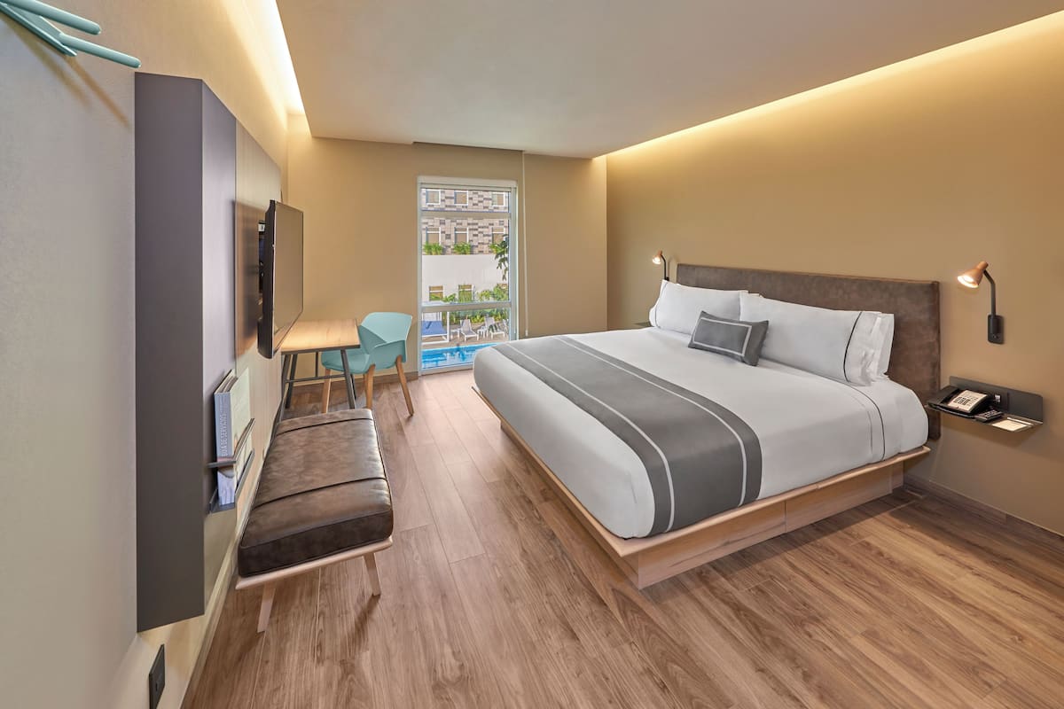 Ein modernes Hotelzimmer mit einem großen Bett, einem Schreibtisch, einem Sessel und einem an der Wand befestigten Fernseher.