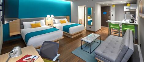 A hotel room with two beds, a desk, a chair, a small table, and a kitchenette.