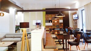 Un hall d’hôtel moderne avec un canapé, un coin repas et un téléviseur fixé au mur.
