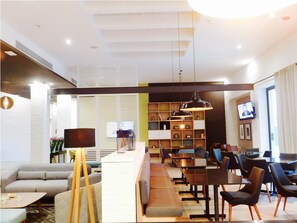 Een moderne hotellobby met een bank, een eethoek en een televisie aan de muur.