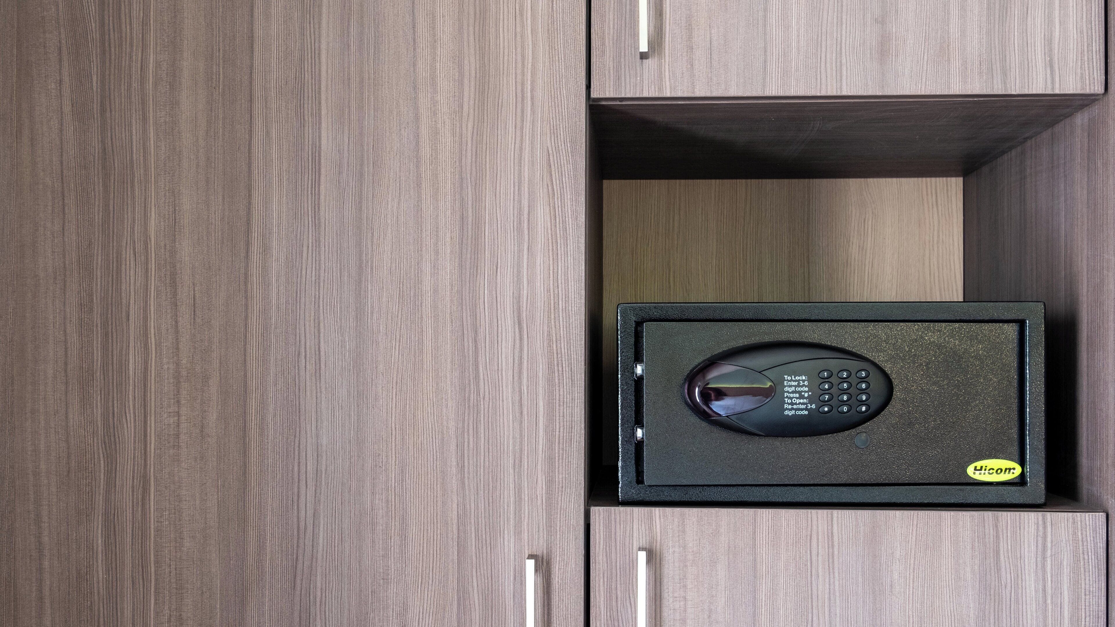 A secure safe with a digital keypad, placed inside a wooden cabinet with a handle.