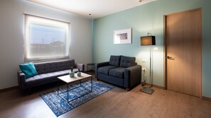 Een woonkamer met een bank, een salontafel, een vloerlamp en een groot raam.