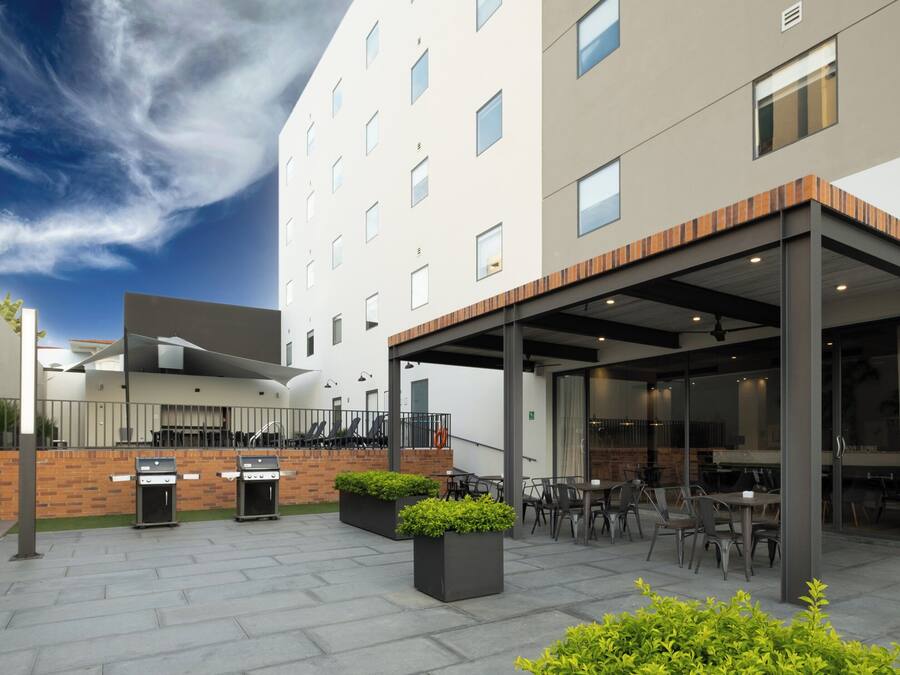 A modern outdoor patio with a covered seating area, outdoor kitchen, and a view of a multi-story building.