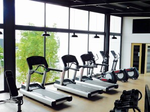 Een sportschool met vier loopbanden, een hometrainer en een halterbank.