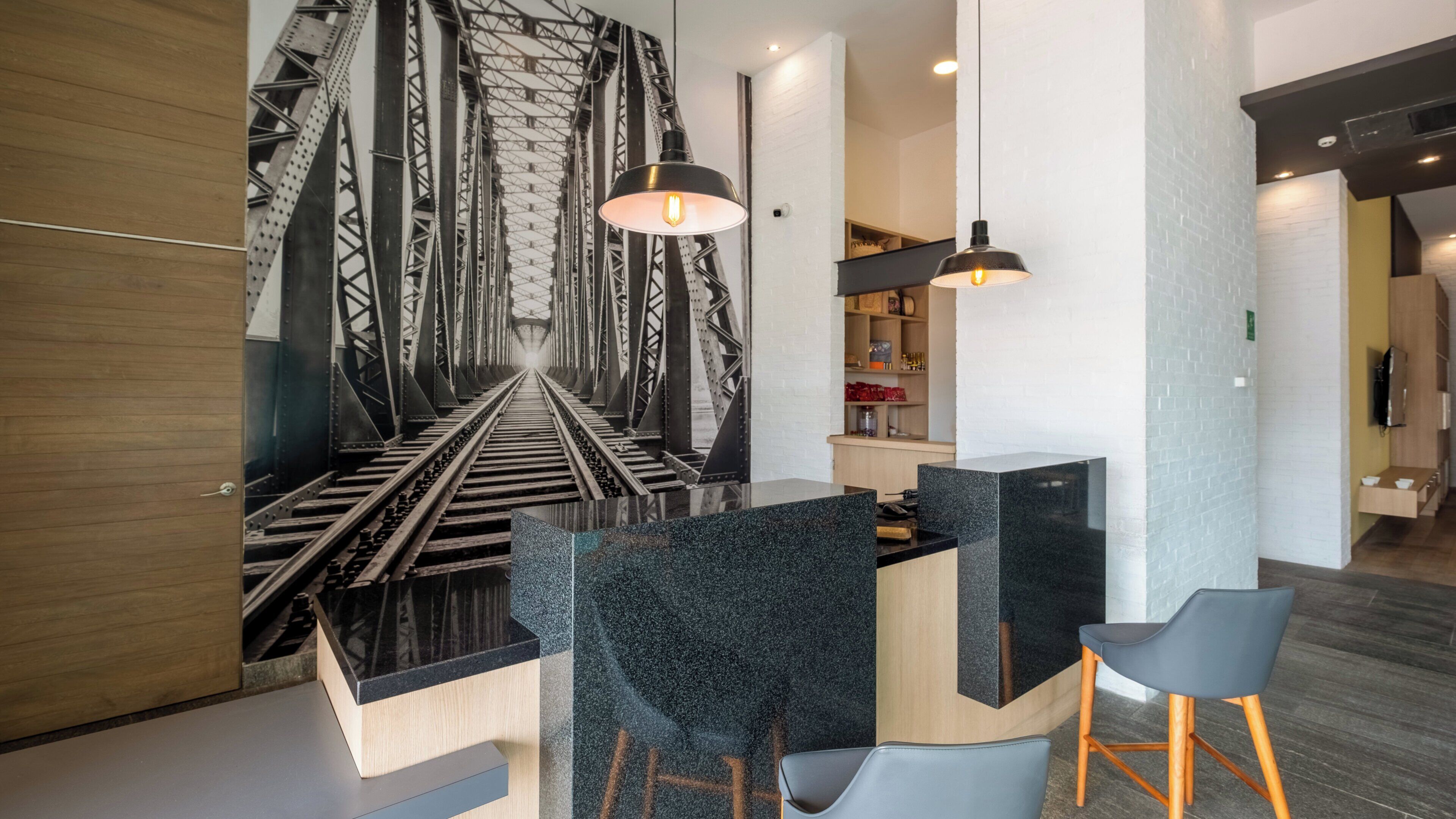 Un interior moderno con un llamativo mural en blanco y negro de una vía de tren, muebles minimalistas e iluminación colgante.