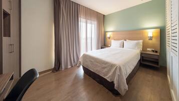 Una camera d'albergo con un letto, una scrivania, una sedia, un comodino e una finestra con tende.