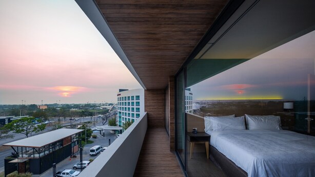 Un balcón con una cama y una mesita de noche, con vistas a un paisaje urbano al atardecer.