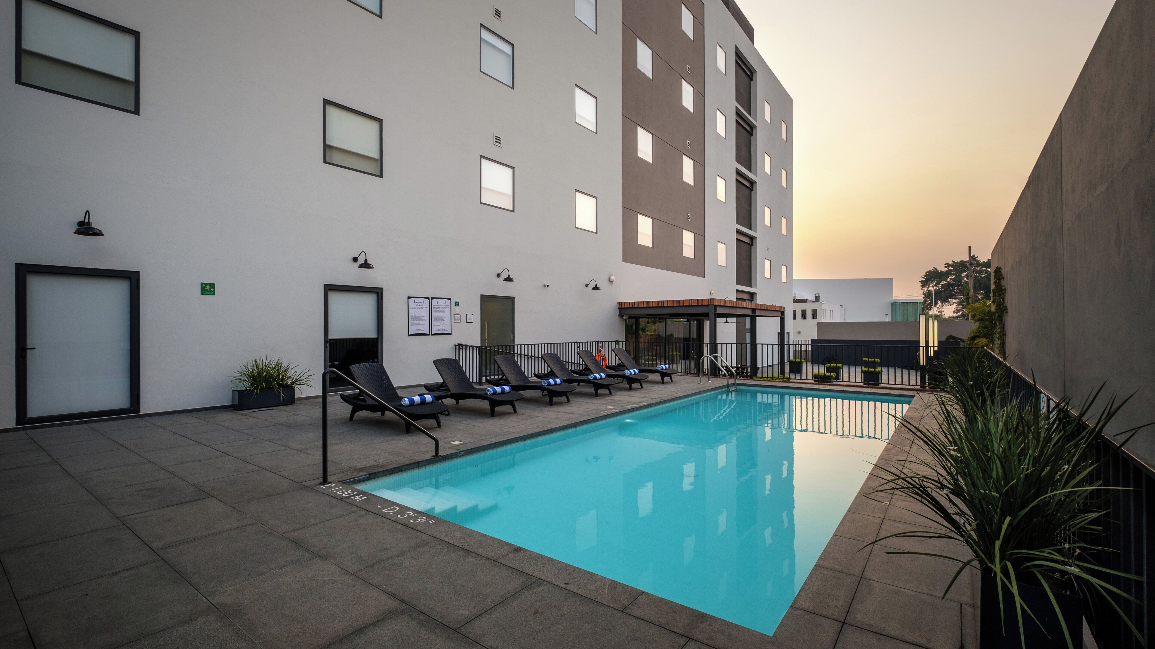 A swimming pool with lounge chairs and a building with multiple windows and doors.