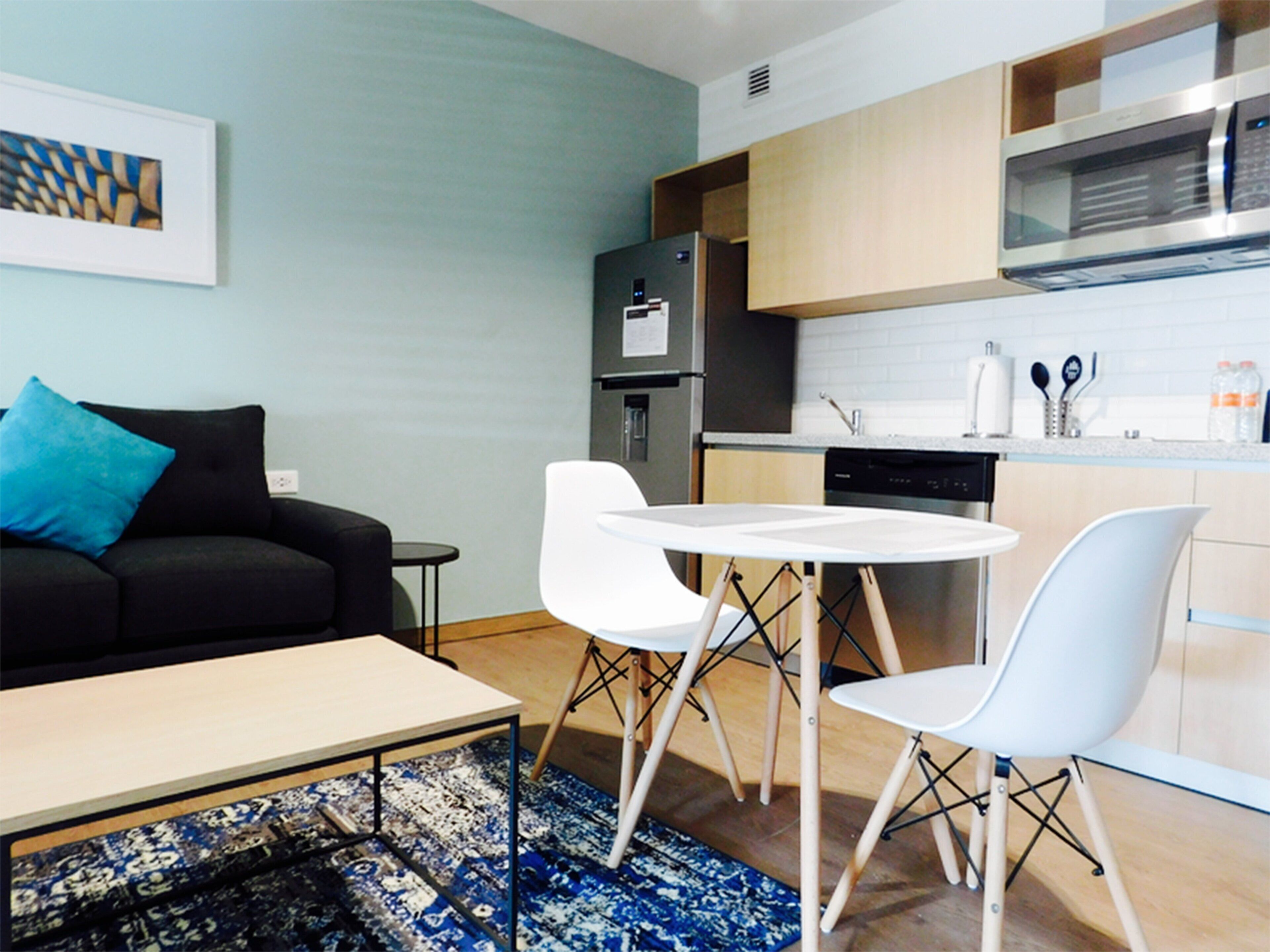 A compact living space with a kitchenette, a dining area with a table and chairs, and a sofa with a blue pillow.