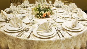 Une table ronde dressée pour un repas formel, avec une nappe blanche, des centres de table floraux et des serviettes soigneusement pliées.