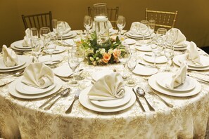 Une table ronde dressée pour un repas formel, avec une nappe blanche, des centres de table floraux et des serviettes soigneusement pliées.