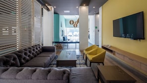 Ein stilvoller Lounge-Bereich mit einer Couch, einem gelben Sessel, einem Couchtisch und einem an der Wand montierten Flachbildfernseher.