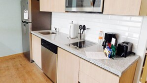 Una cocina compacta equipada con lavavajillas integrado, refrigerador de acero inoxidable, microondas, pileta con grifo y tostadora.