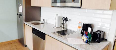 A compact kitchen with a built-in dishwasher, a stainless steel refrigerator, a microwave, a sink with a faucet, and a toaster.