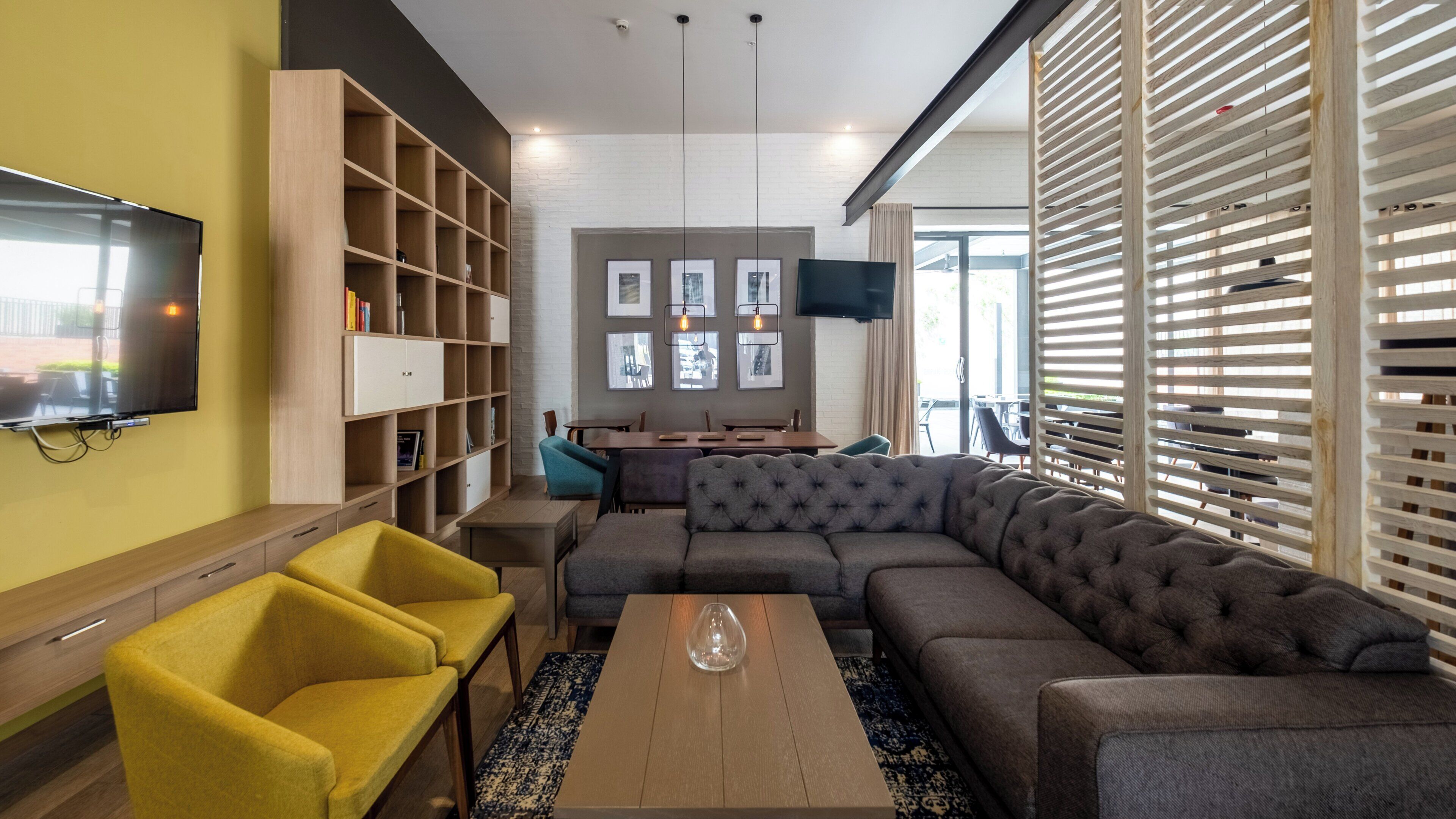 Un salon moderne avec un canapé d’angle, des fauteuils jaunes, une table basse, une bibliothèque et un téléviseur à écran plat.