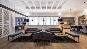 Un salon moderne avec un canapé, deux tables d’appoint et une table basse. Il y a également un coin cuisine avec un bar et des tabourets.