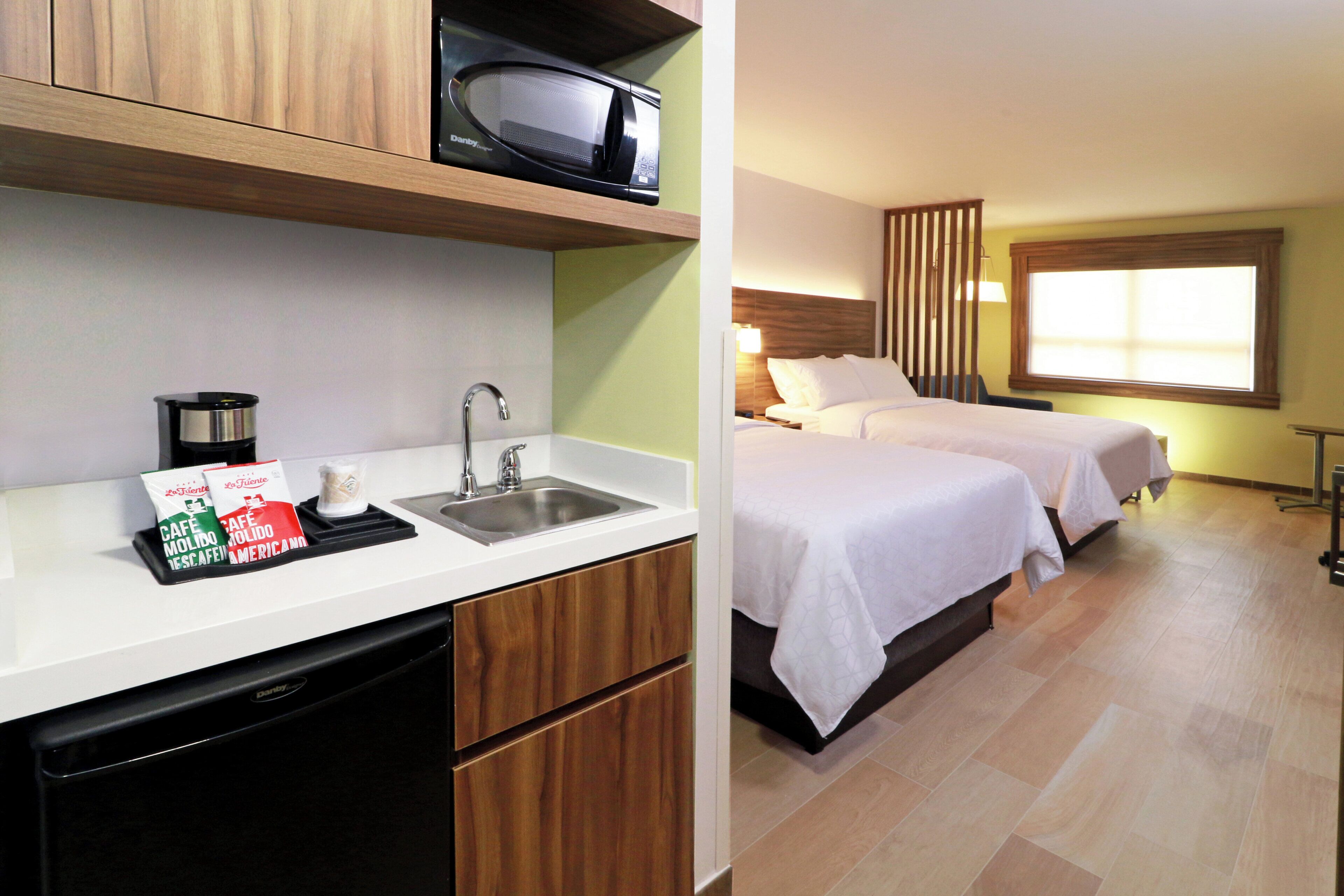 A hotel room with a kitchenette, a sink, and two beds.