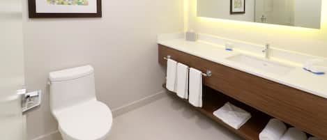 A modern bathroom with a toilet, a vanity with a mirror, and a shelf with towels.