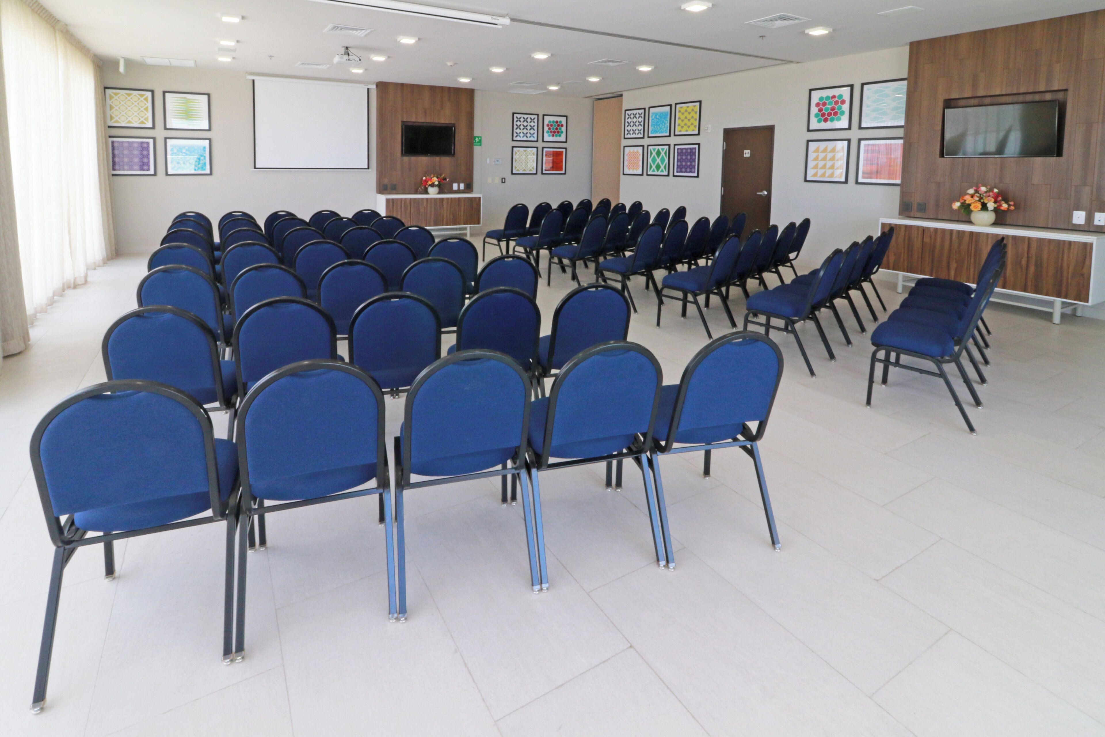 A conference room with rows of blue chairs, a whiteboard, and a television on a wooden cabinet.