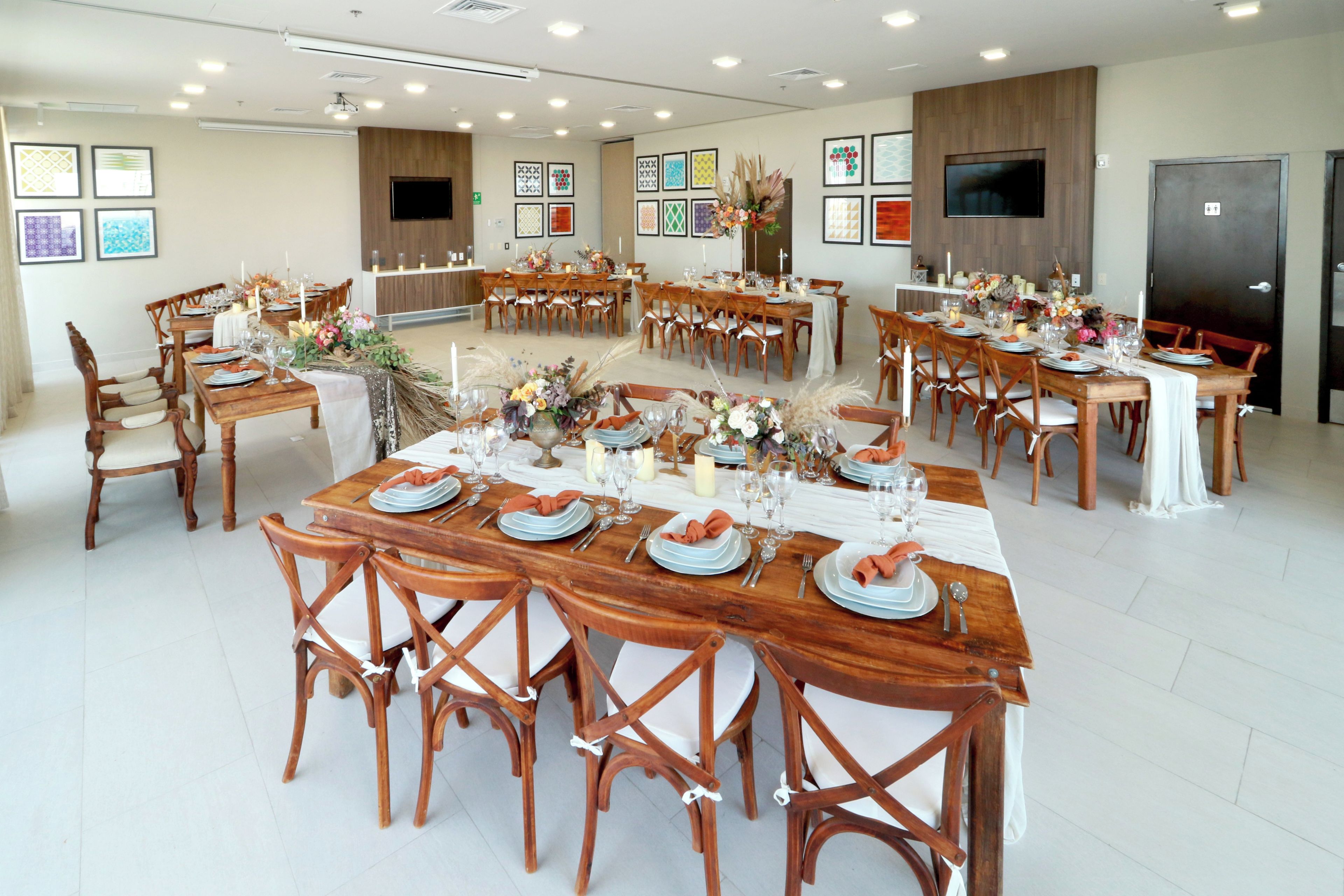 Une grande salle à manger, dotée de nombreuses tables dressées pour le repas, de chaises en bois et d’œuvres d’art encadrées accrochées aux murs.
