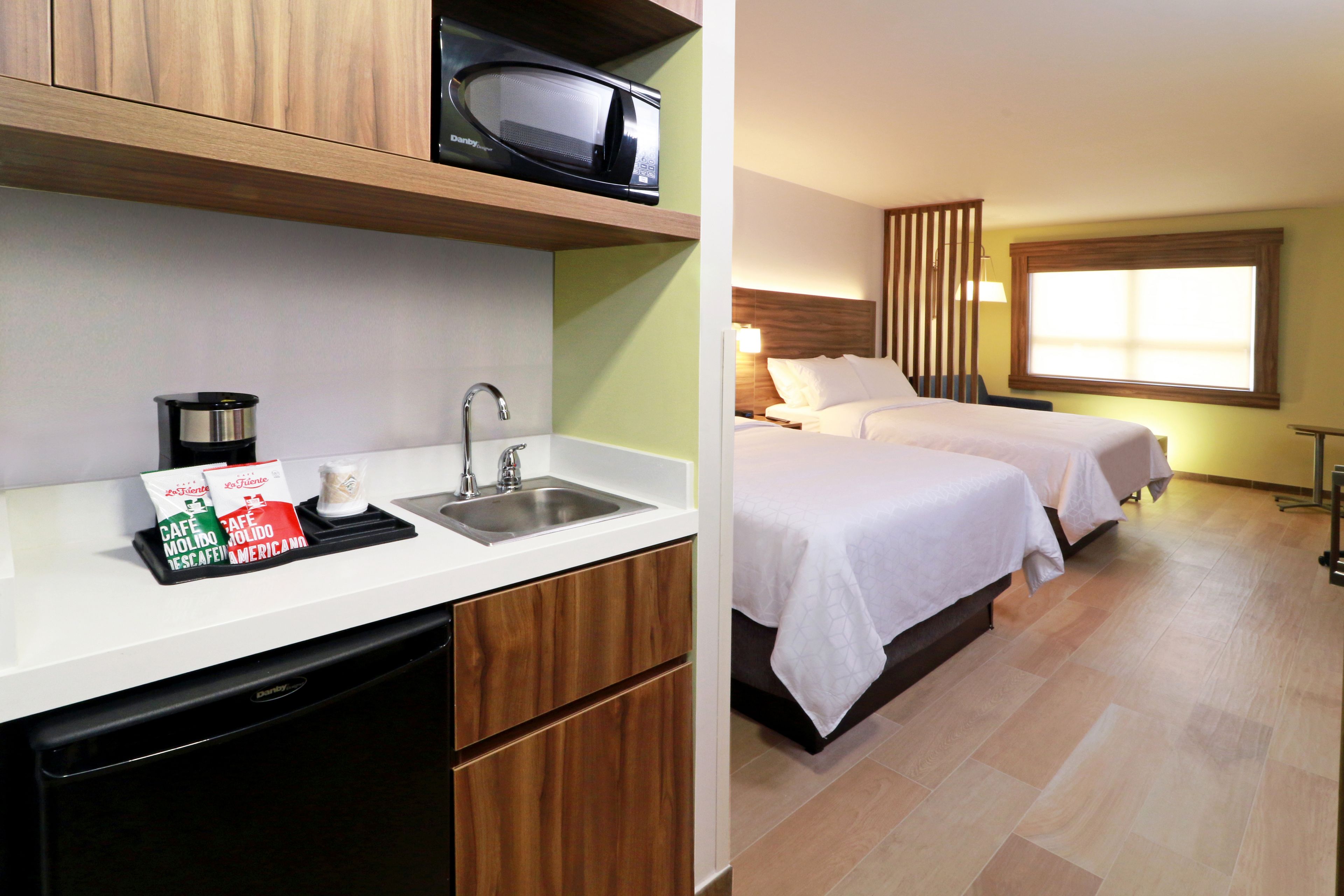 A hotel room with a kitchenette, a bed, and a window.