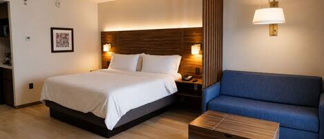 A hotel room with a bed, bedside table, lamp, and a blue sofa.