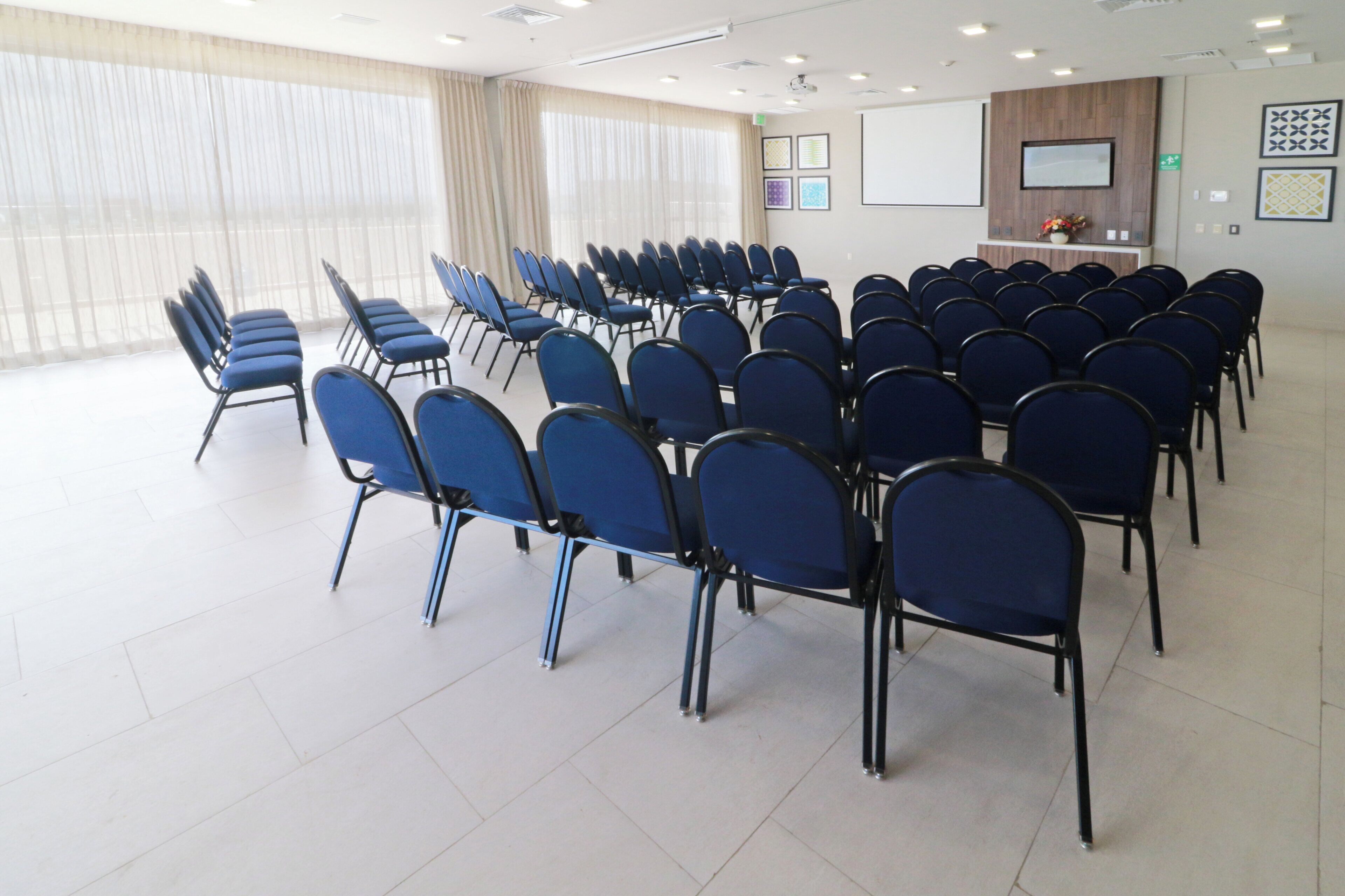 Une salle de conférence avec des rangées de chaises bleues, un tableau blanc et des tableaux encadrés accrochés au mur.