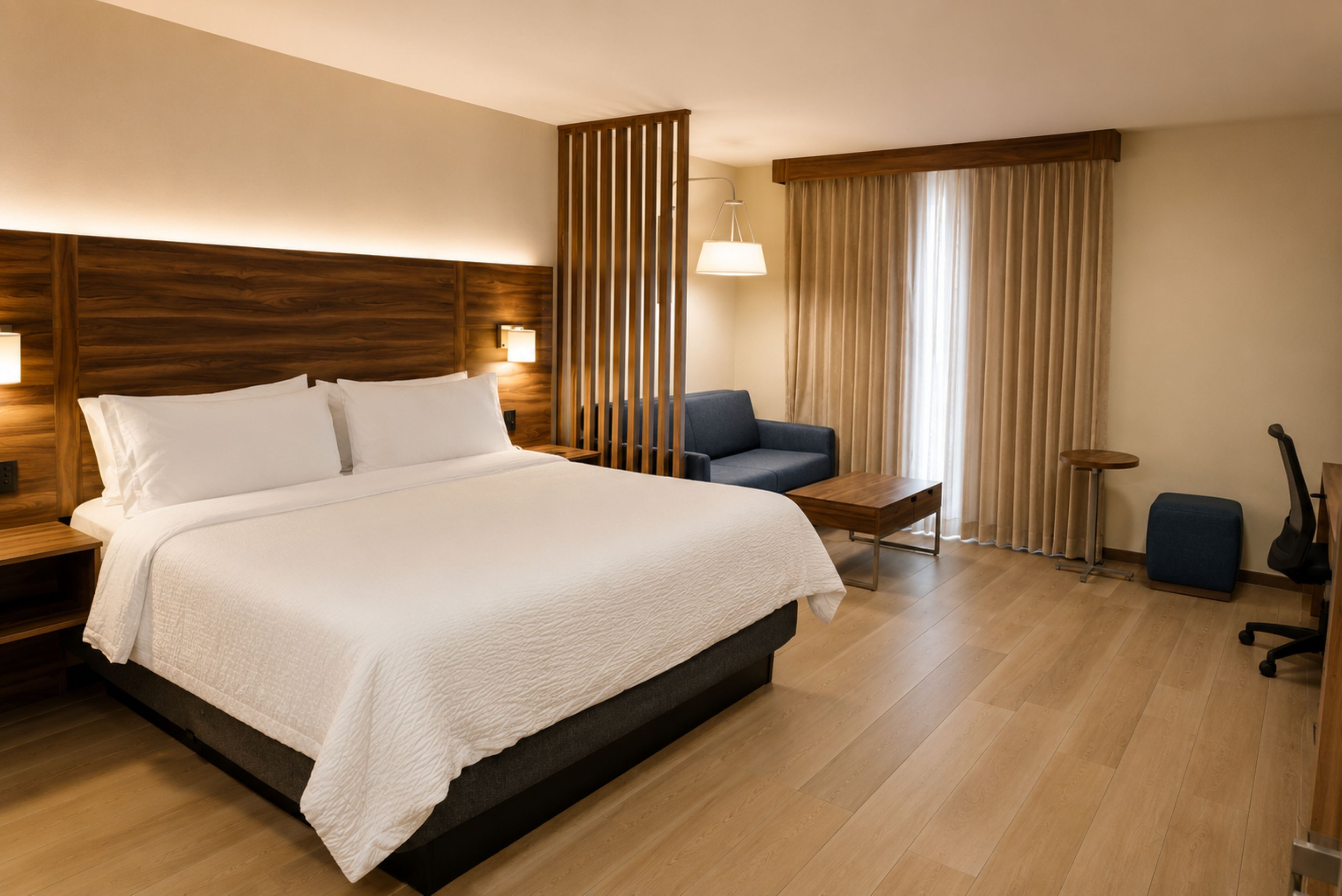A hotel room with a large bed, a desk, a chair, a lamp, and a window with curtains.