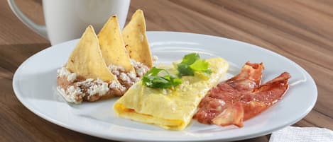 Un plato con tortilla, tocino y totopos sobre una mesa de madera.