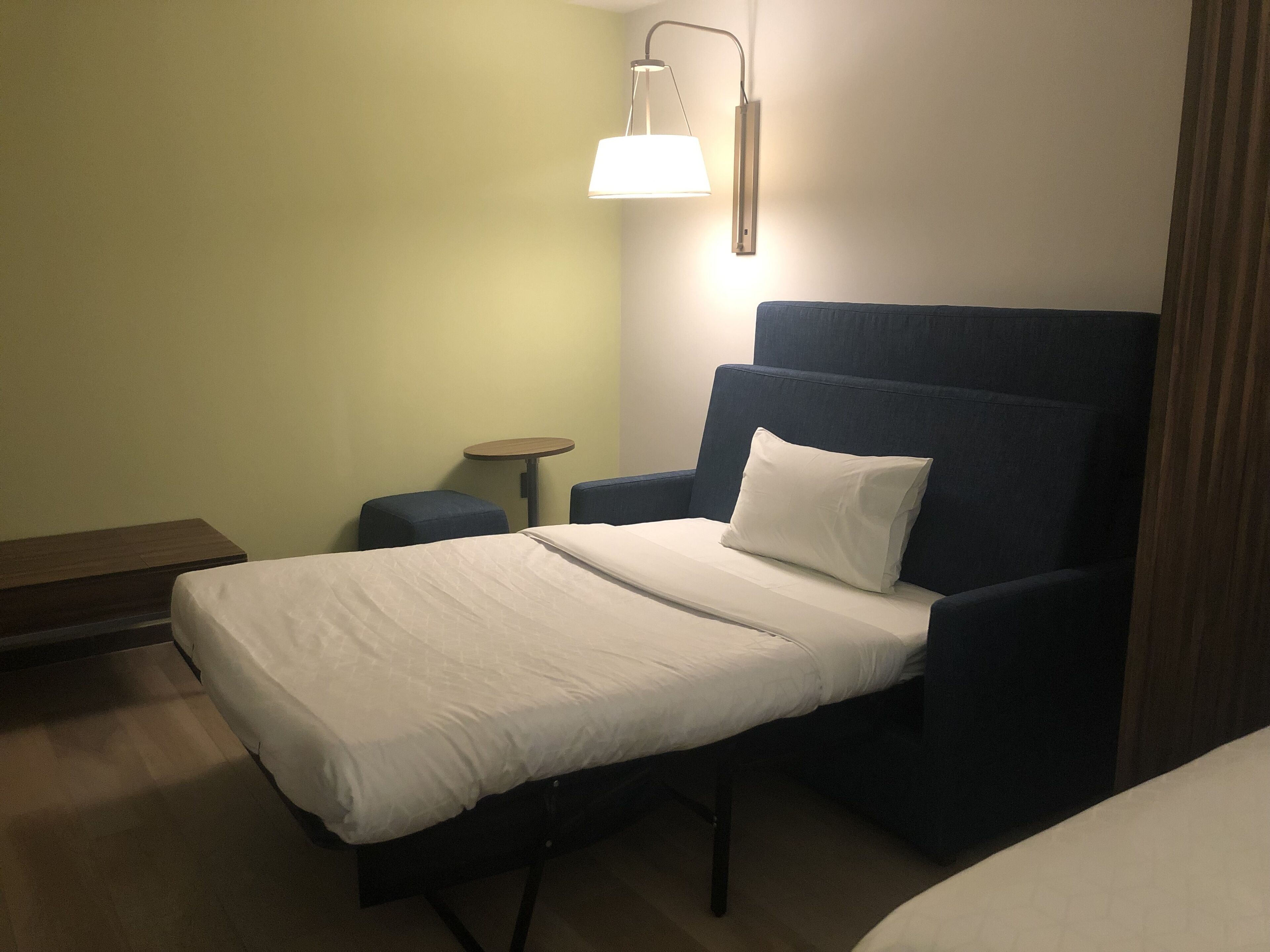 Ein Hotelzimmer mit einem Einzelbett, einem kleinen runden Tisch und einem blauen Sessel.