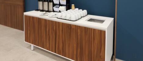 A buffet setup with a white counter, food containers, and a coffee station.