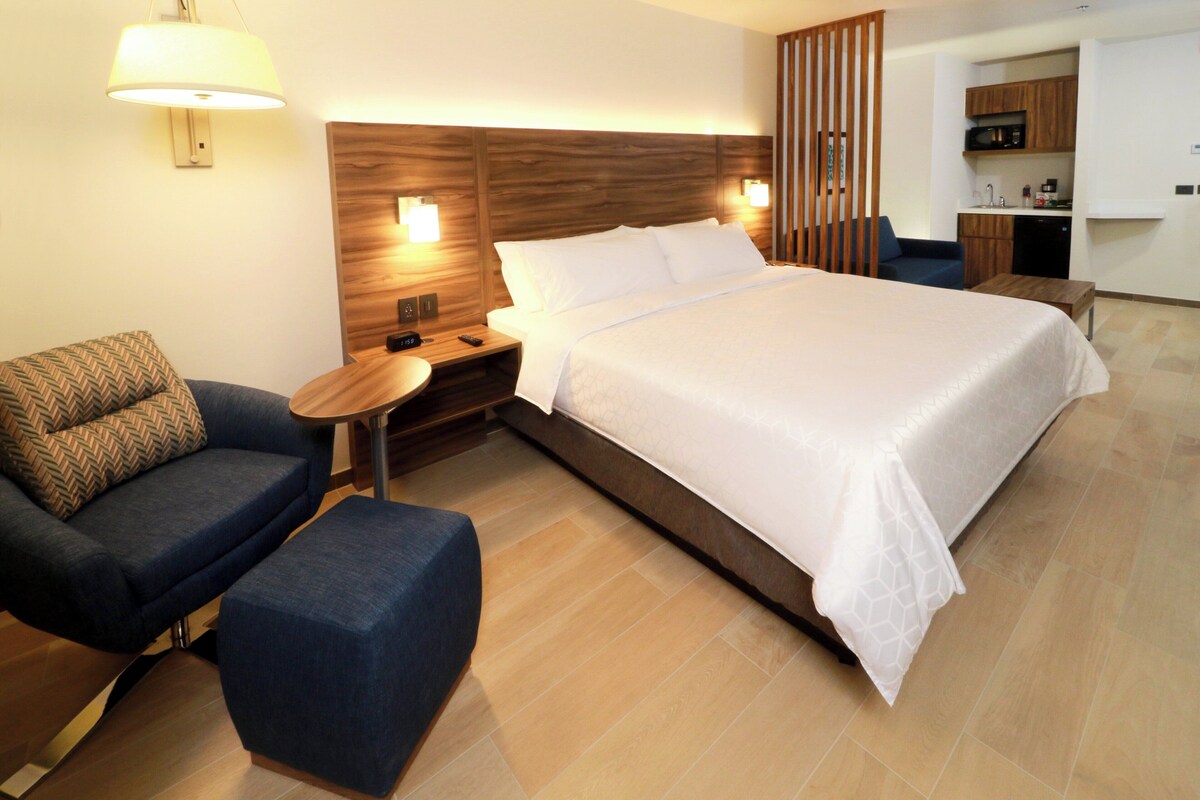 Ein Hotelzimmer mit Bett, Sofa, einem kleinen Tisch, einer Lampe und einer Küchenzeile.