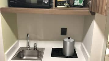 Una cocina compacta con microondas, cafetera y dispensador de cápsulas de café en la encimera.