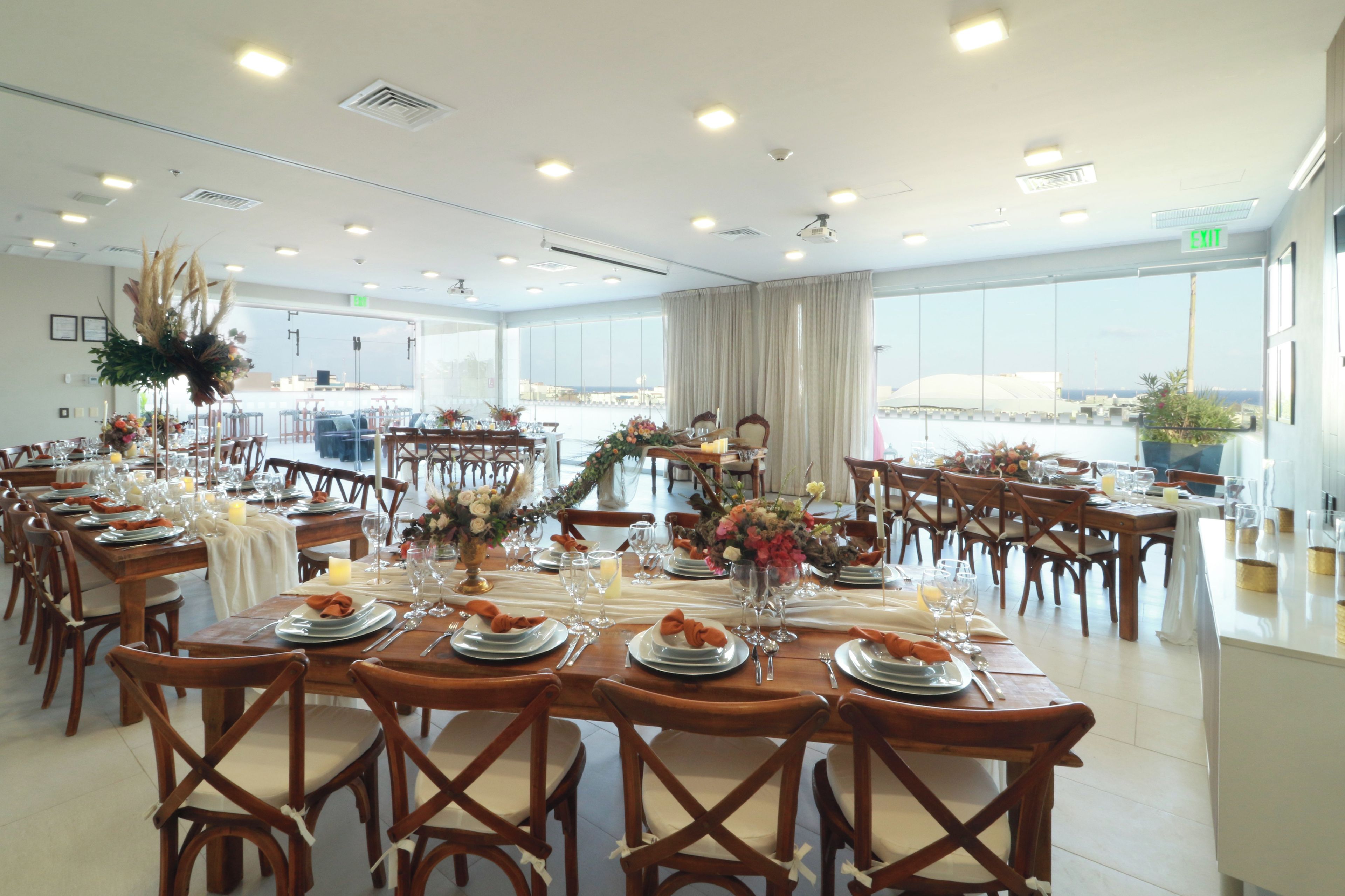 A spacious dining area with multiple tables set for a meal, large windows offering a view, and a modern ceiling design.