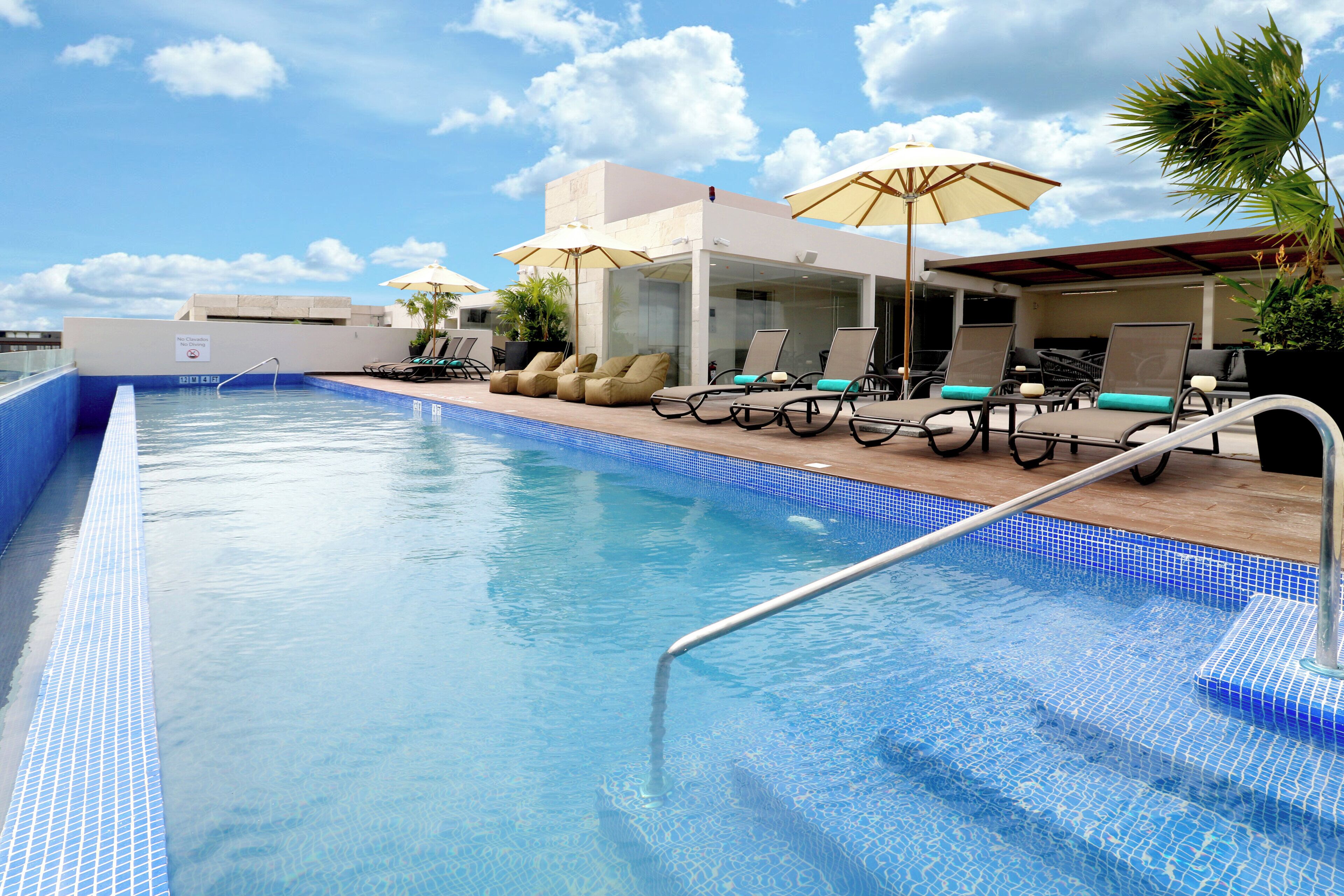 A swimming pool with lounge chairs and umbrellas, surrounded by a building with a tiled roof.