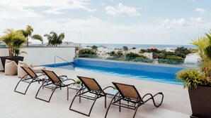 Une piscine sur le toit, agrémentée de chaises longues, offrant une vue dégagée sur la mer, et avec une enseigne d ’hôtel en arrière-plan.