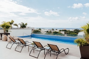 Une piscine sur le toit, agrémentée de chaises longues, offrant une vue dégagée sur la mer, et avec une enseigne d’hôtel en arrière-plan.