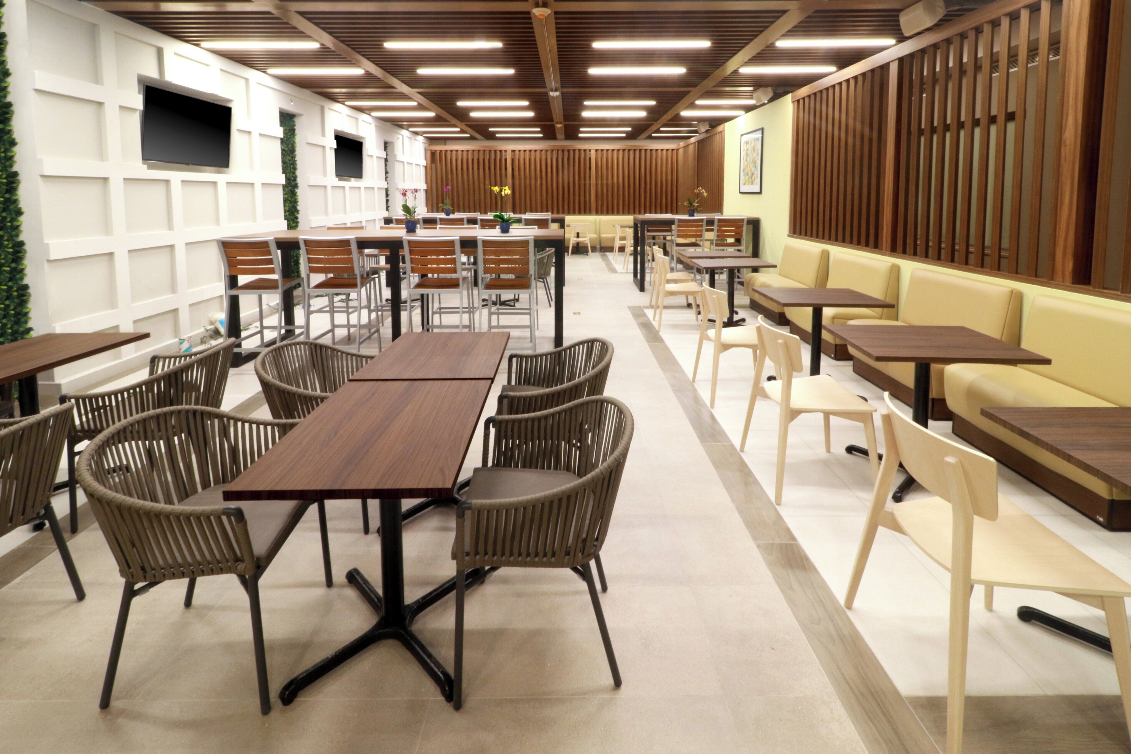 A spacious indoor dining area with multiple tables and chairs, wooden paneling on the walls, and a ceiling with linear lighting fixtures.