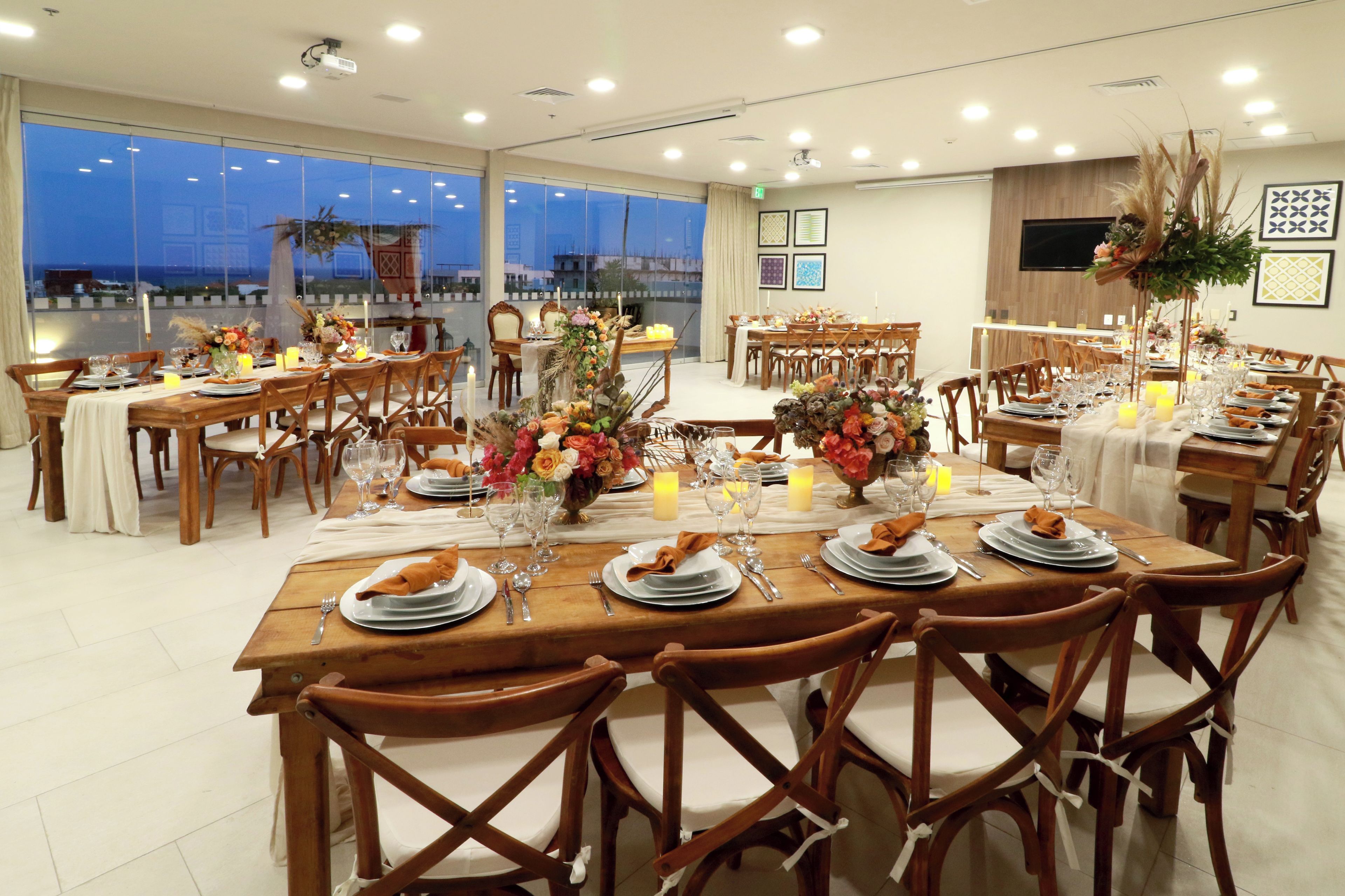 Un comedor amplio con varias mesas dispuestas para una comida, con mobiliario de madera y vistas al exterior.