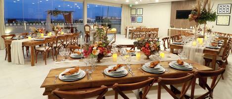 A spacious dining area with multiple tables set for a meal, featuring wooden furniture and a view of the outdoors.