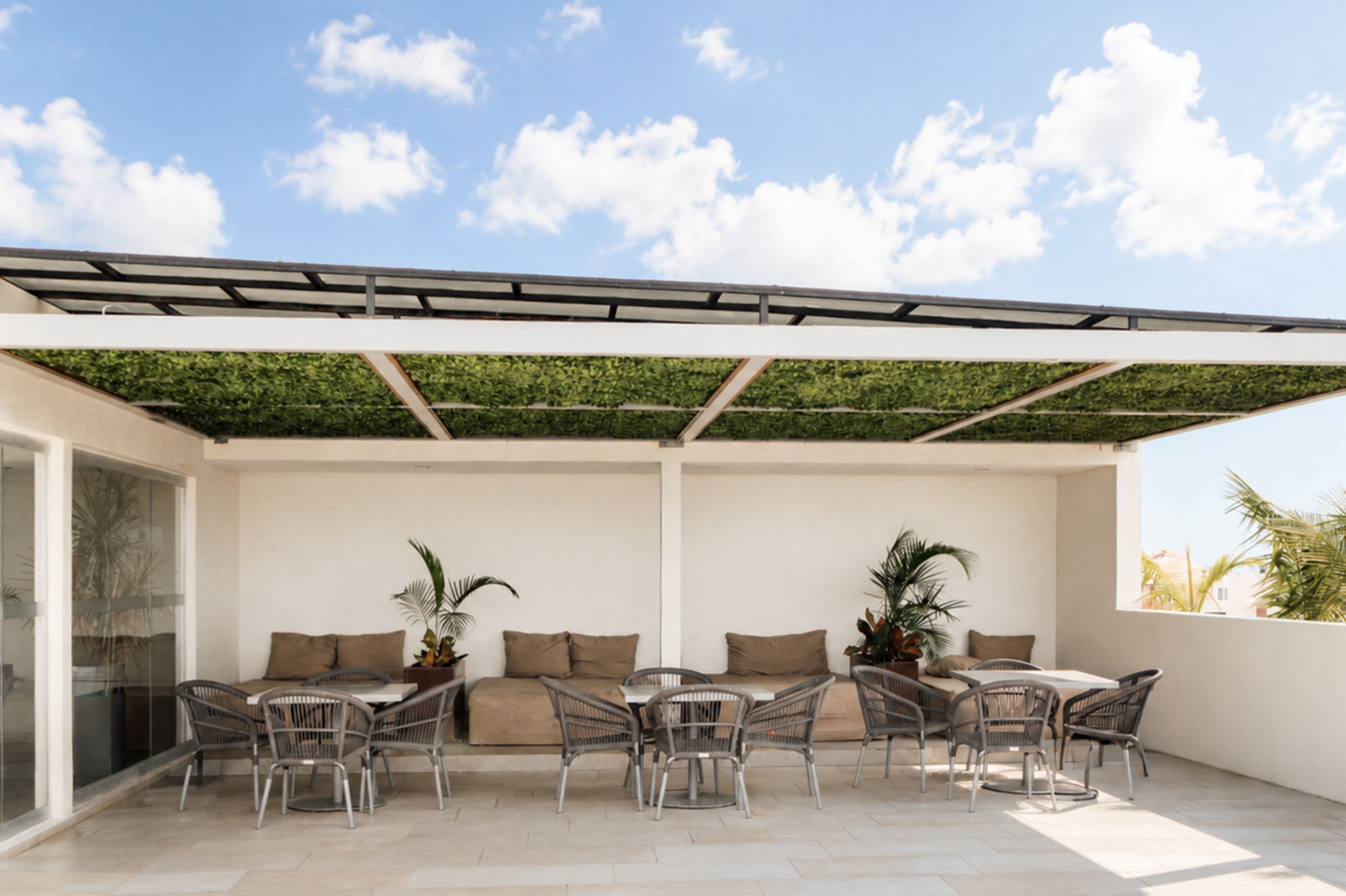 Patio esterno con zona salotto coperta, comprendente un divano e sedie da pranzo, sotto una pergola con tetto verde.